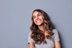 woman smiling on gray background for teeth cleaning Sugar Land texas services including teeth cleaning and dental exams