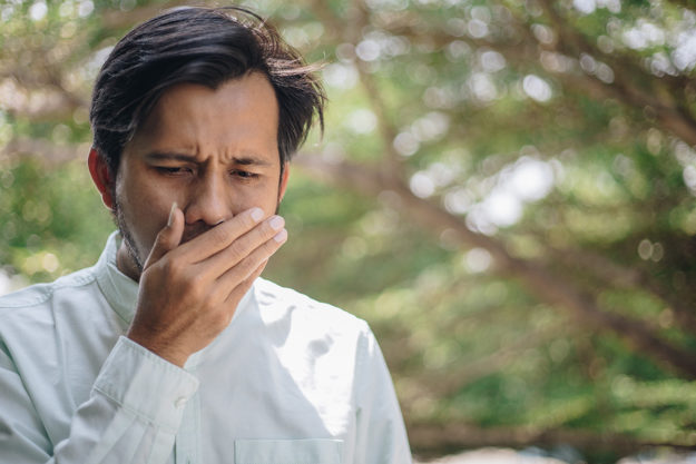 causes of bad breath man covering his mouth with his hand to check breath worried about the Causes of Bad Breath