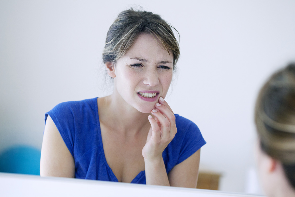 woman looking in the mirror at painful tooth wondering How Does Tooth Decay Develop
